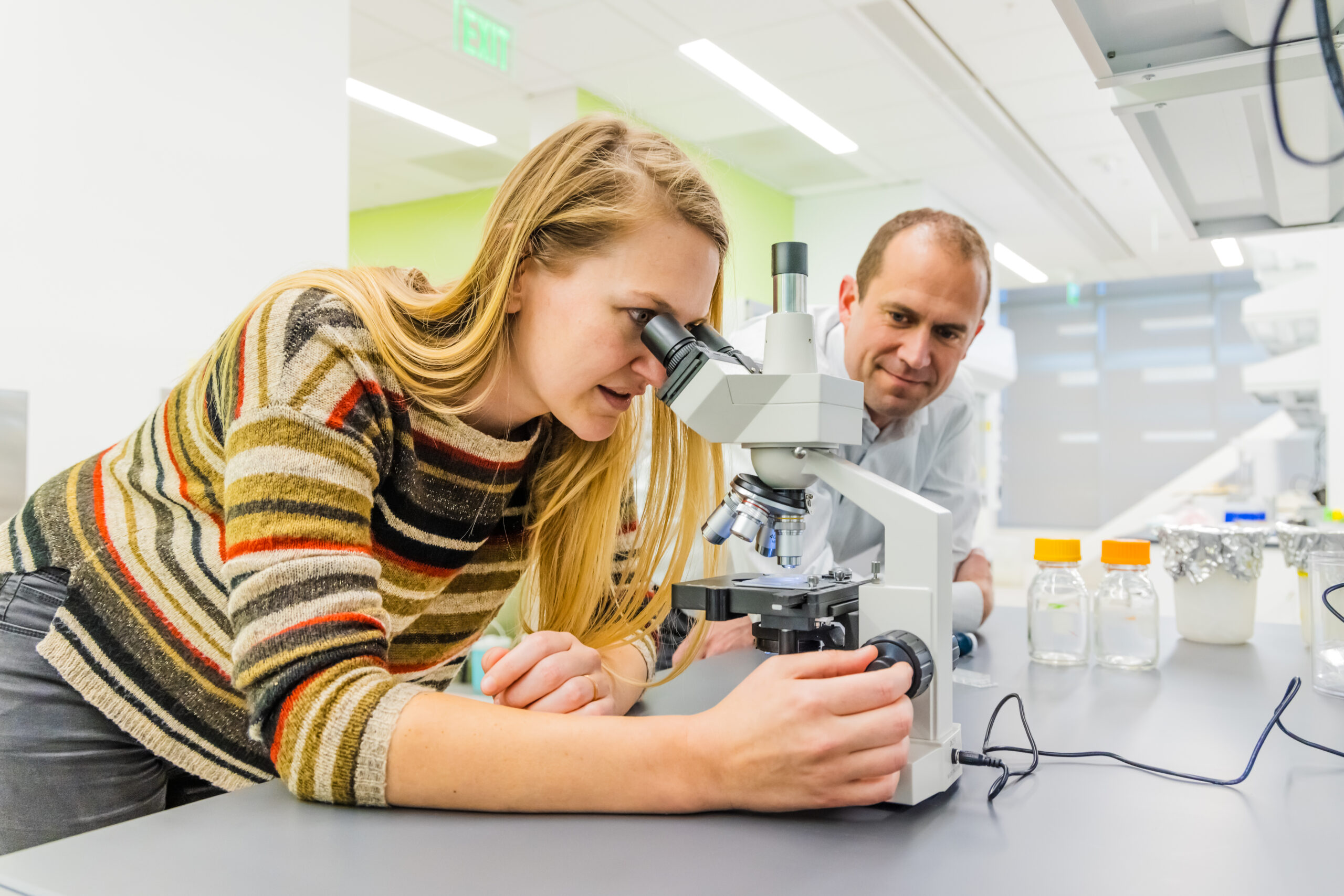 Director Jacob Jones with scholar looking at microscope in the lab.